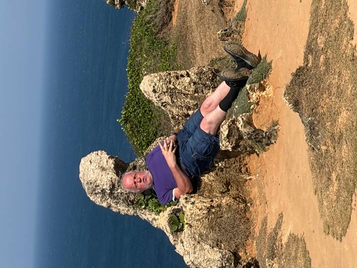 A man relaxes on a natural stone seat overlooking the blue sea and rugged coast.