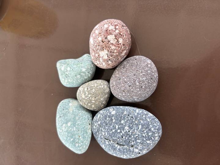 Six polished, multicoloured pebble stones displayed on a brown tabletop.