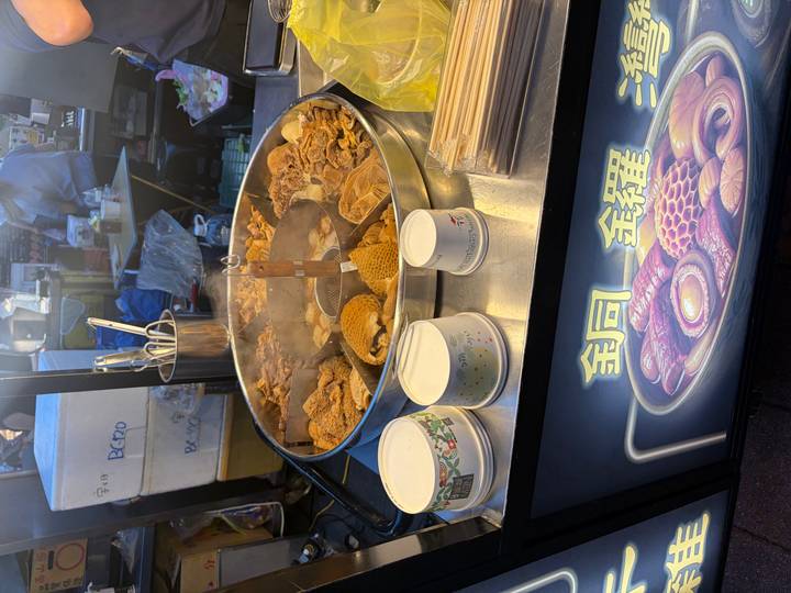 A steaming metal basin filled with assorted braised meats at a busy night market stall.