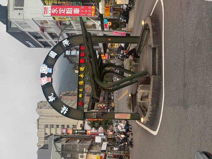 An arched green steel bus shelter with colourful LED text stands on a small-town street.
