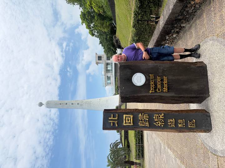 Man beside stone pillars marking the Tropic of Cancer monument under a partly cloudy sky.
