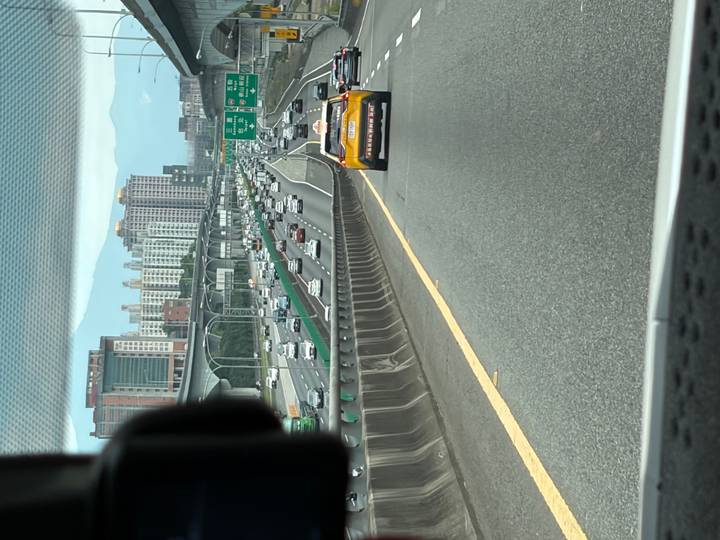 View from a vehicle of busy multilane highway traffic leading toward city high-rises and mountains.
