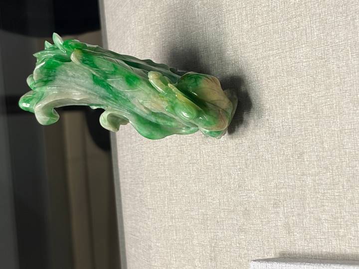 A small jadeite carving resembling a cabbage displayed on a neutral fabric surface.