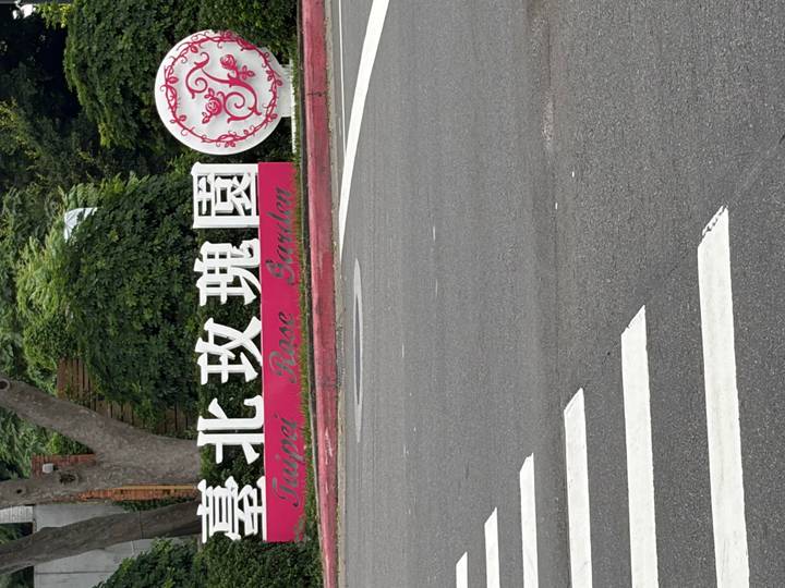 Sign reading "Taipei Rose Garden" beside a roadway and crosswalk.