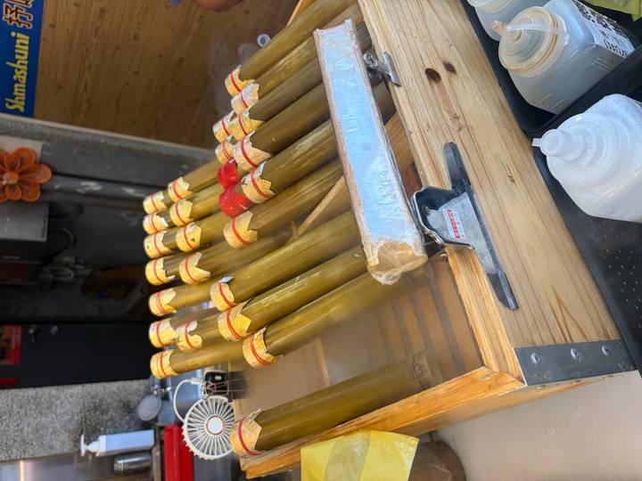Steaming bamboo tubes of sticky rice arranged in a wooden tray at a street vendor.