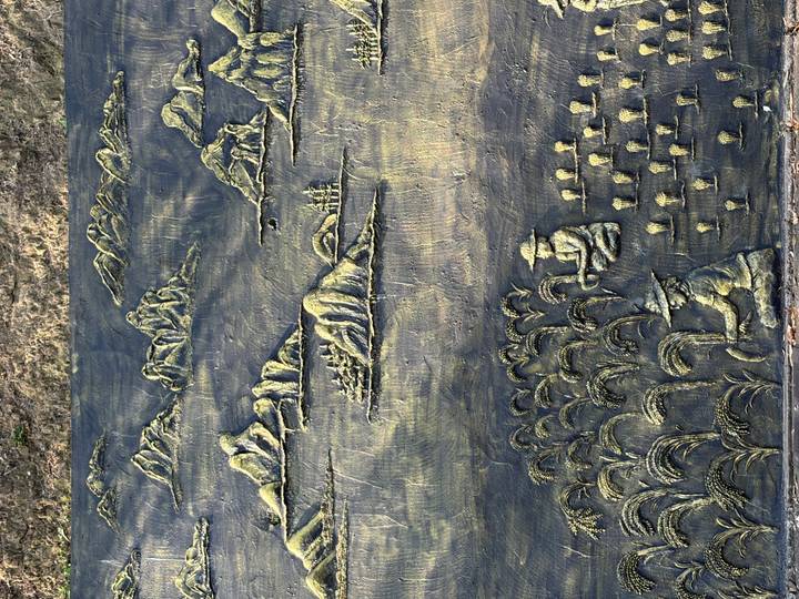 Bronze relief panel depicting rice fields, farmers, and mountains in shallow perspective.