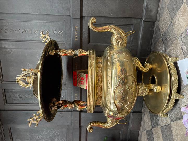 An ornate gold incense burner with intricate reliefs stands before dark temple doors.