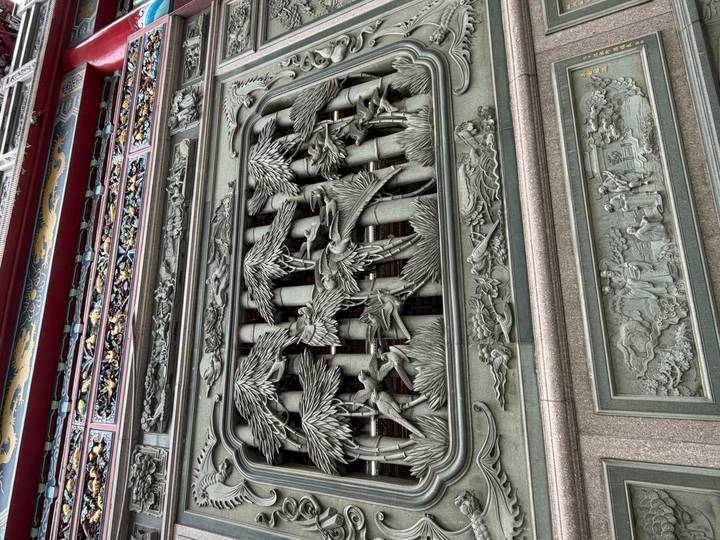 Detailed stone carving on a temple façade depicting birds among bamboo and figures below.
