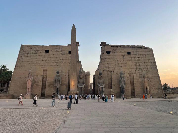 Luxor Temple entrance with obelisk at dusk, softly lit with tourists gathering in the courtyard.