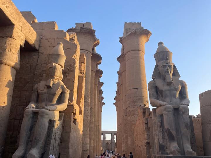 Golden-hour light falls on two colossal seated pharaoh statues flanking temple columns.