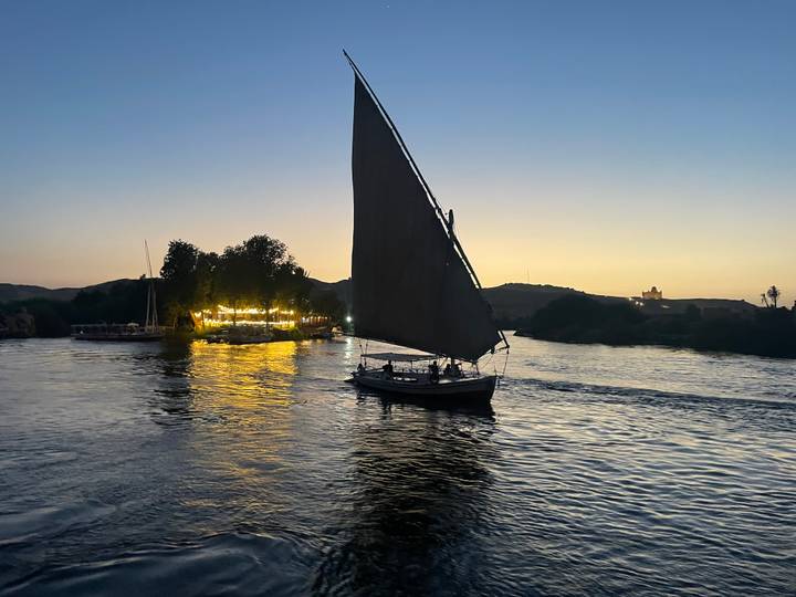 Silhouette of a traditional felucca sailing on the Nile at sunset with reflections of golden light on the water.