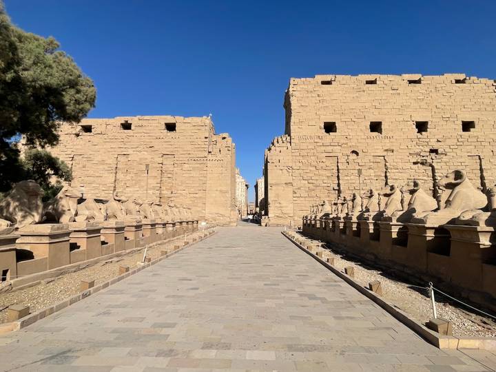 Symmetrical avenue of ram-headed sphinxes leading to the first pylon of Karnak Temple beneath a clear blue sky.