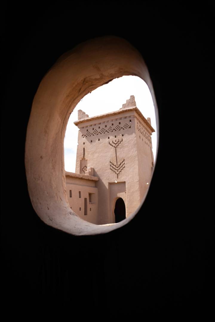 Mud-brick watchtower with geometric motifs seen through a rounded adobe window opening.