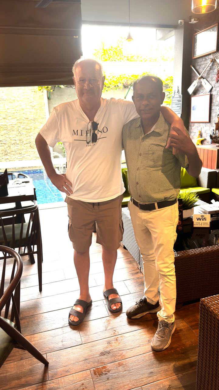 Two travelers pose together in an indoor lounge area beside a swimming pool.