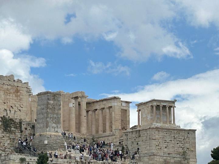 Ancient marble columns and temple ruins atop the Athens Acropolis beneath blue sky.