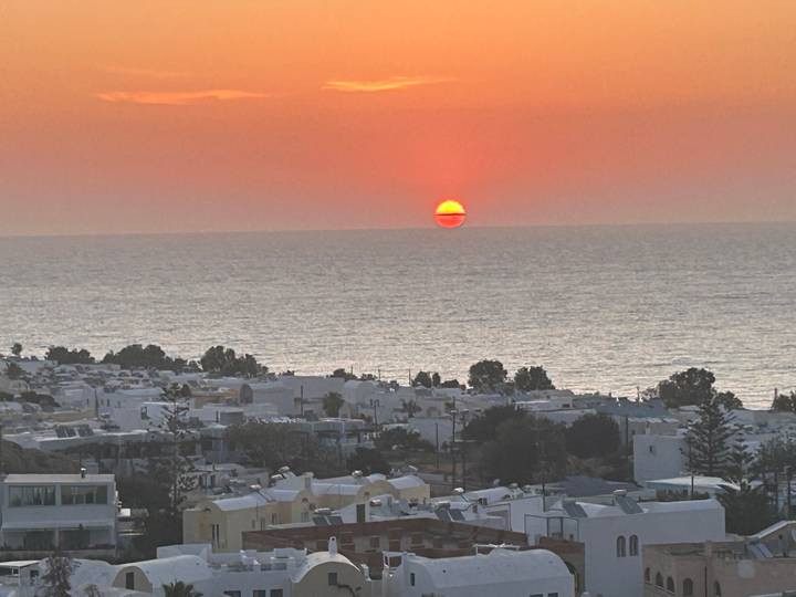 Bright orange sun setting into the Aegean Sea over whitewashed Santorini rooftops.
