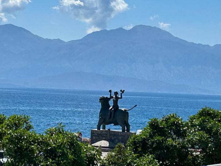 Bronze statue of Europa riding the bull by the sea with mountains in the background on Crete.