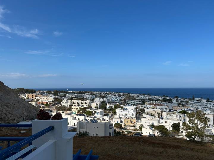 Wide view of a whitewashed village spreading toward the Aegean Sea under a clear blue sky.