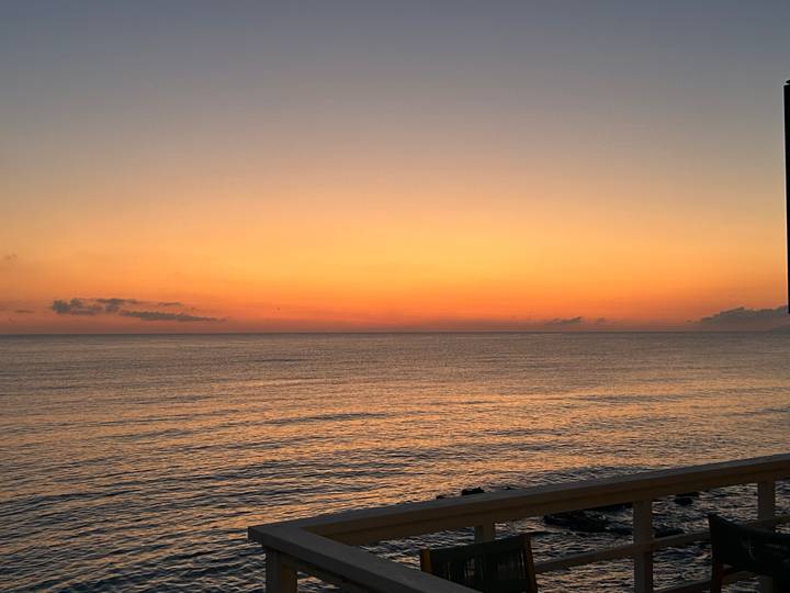 Orange dusk sky over a calm open sea viewed from a balcony railing.