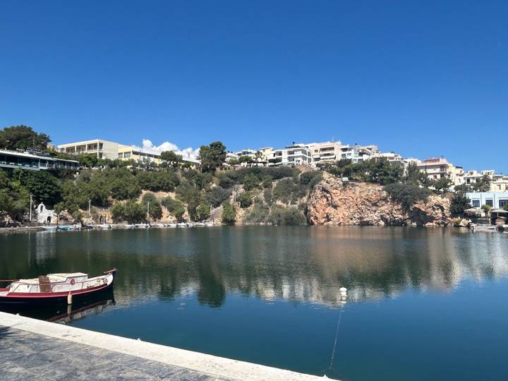 Calm lake surrounded by town buildings and cliffs reflecting in the water on a sunny day.