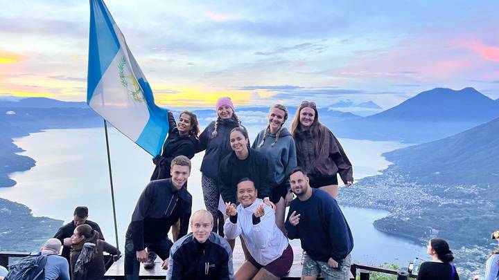 Happy group posing with national flag atop viewpoint overlooking Lake Atitlán at sunrise