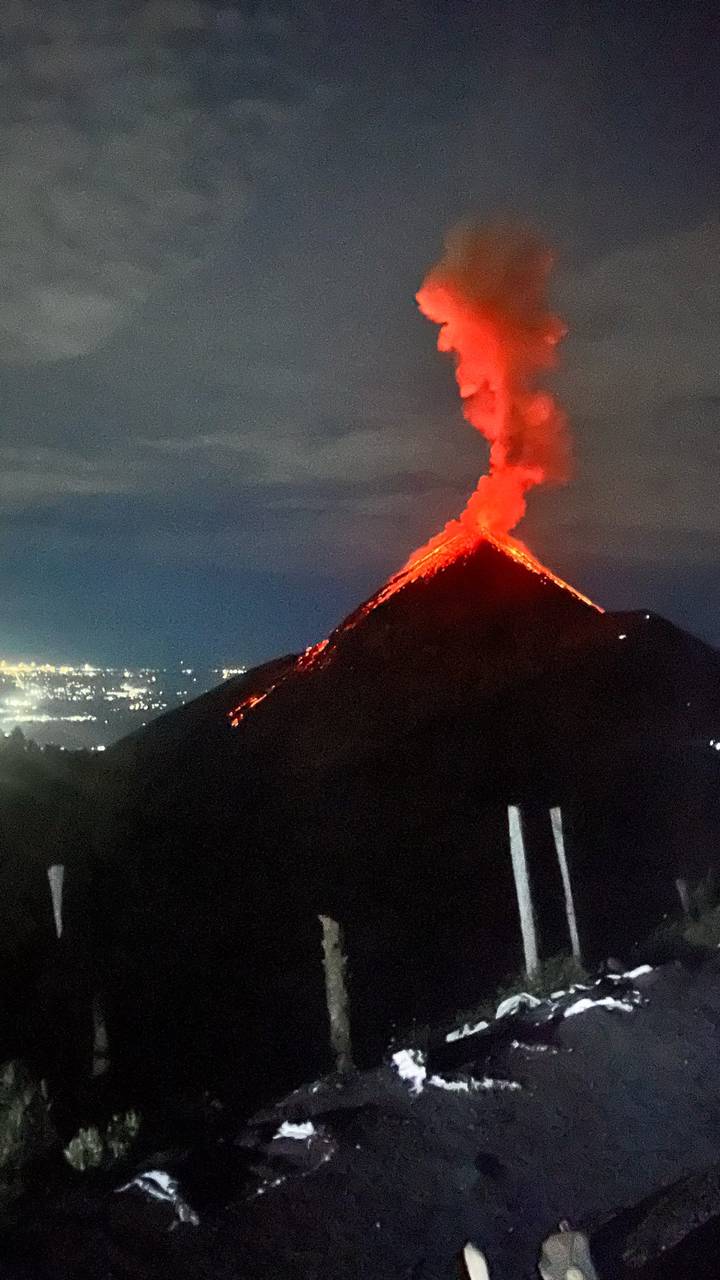 Nighttime eruption of volcano with bright red lava rivers against dark sky