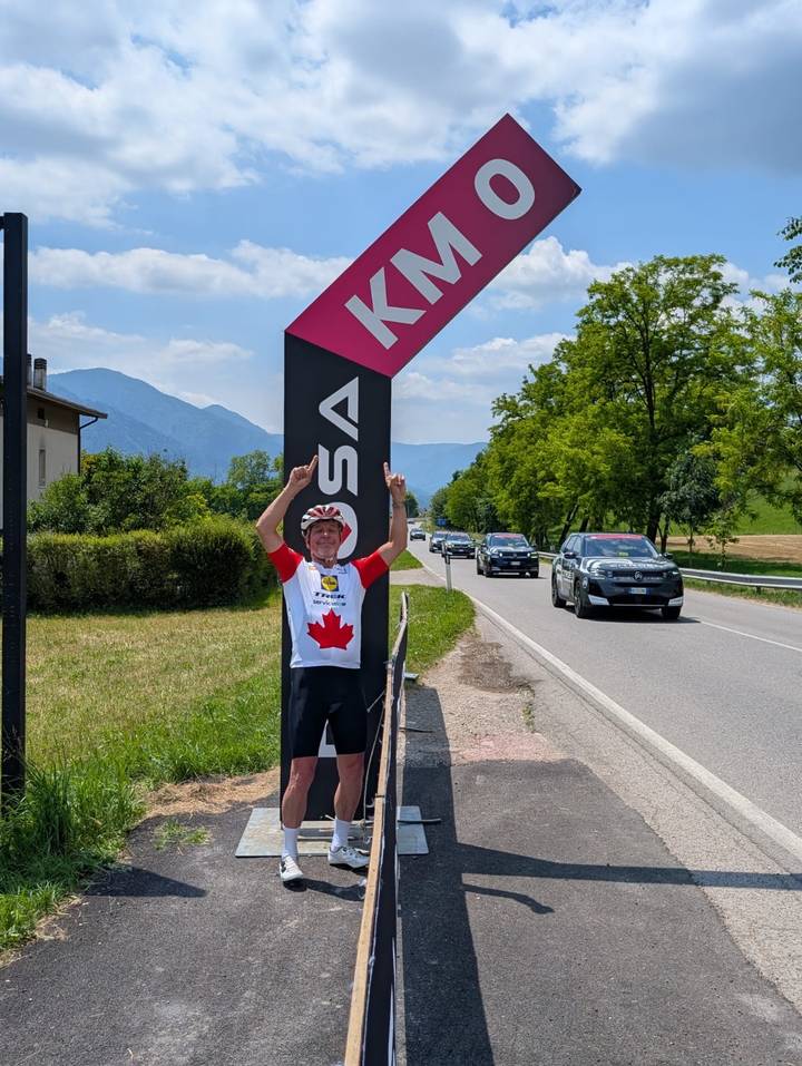 Cyclist celebrating at roadside Rosa banner with mountain scenery behind