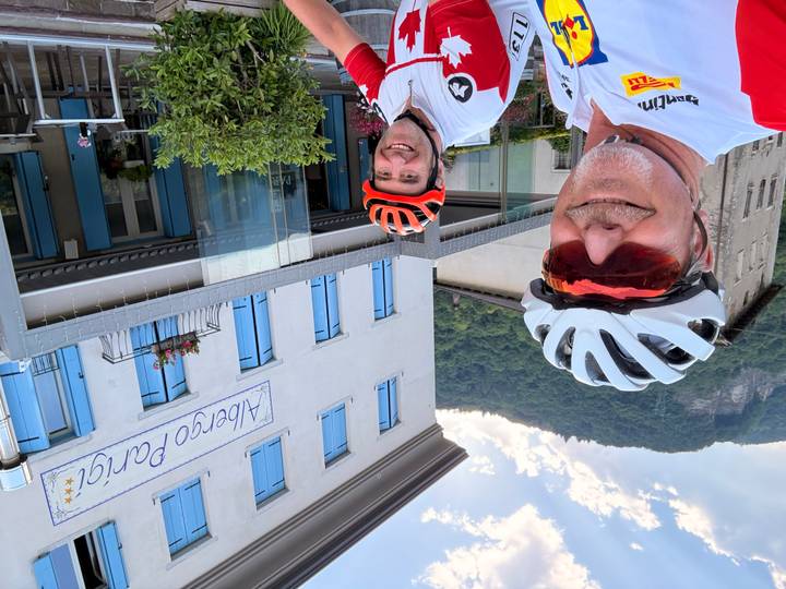 Two cyclists smiling outside Albergo Parigi hotel with forested hillside backdrop