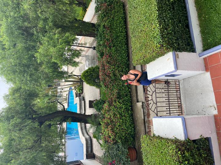 Woman smiling behind a small gate in a lush courtyard with a swimming pool in the background