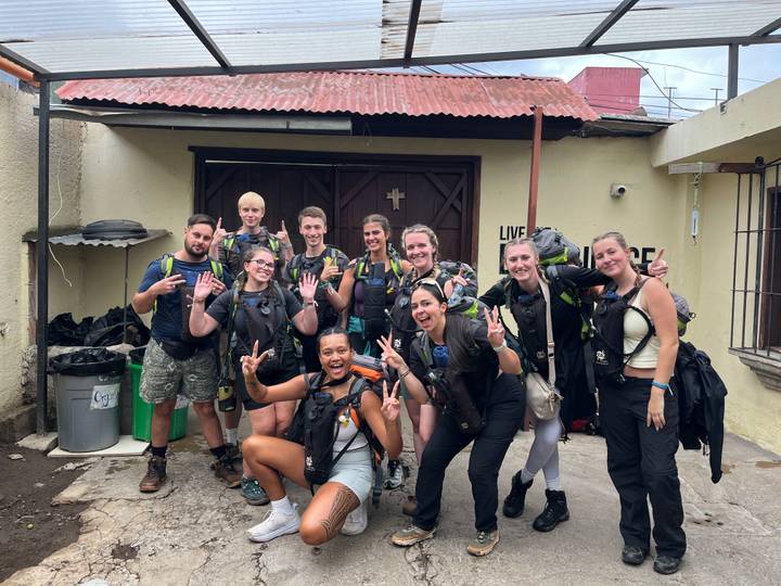 Large group of trekkers in hiking gear posing outside a building before a climb