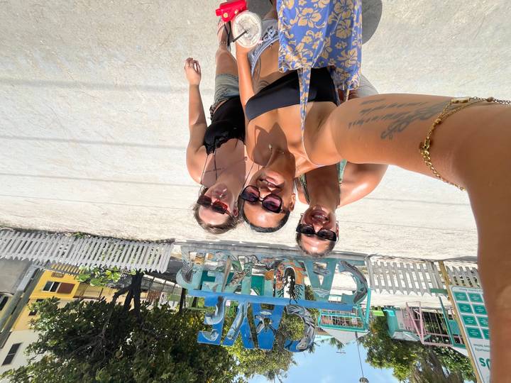 Three women taking a selfie in front of the colorful 'Caye Caulker' sign