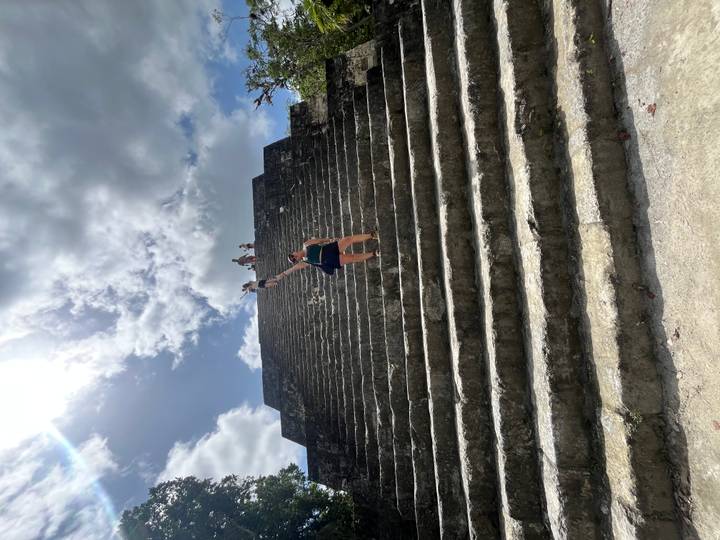 Woman halfway up massive stone pyramid steps with others at the top under bright sun