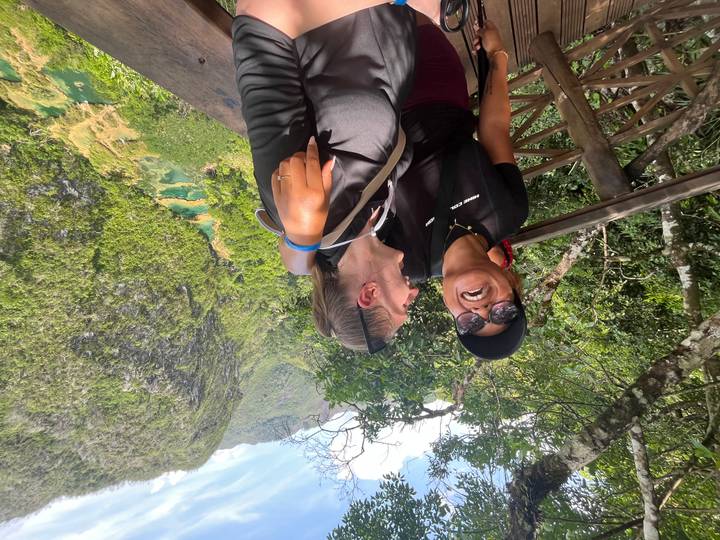 Two women laughing on a wooden lookout over lush green valley and turquoise pools