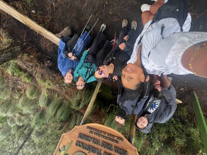Selfie of hikers in rain gear on a muddy trail surrounded by tall grasses