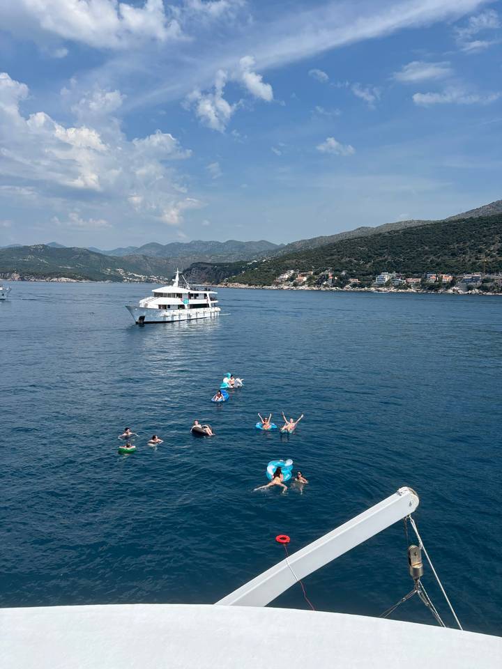 Small cruise boat anchored while swimmers float and relax in clear Adriatic waters
