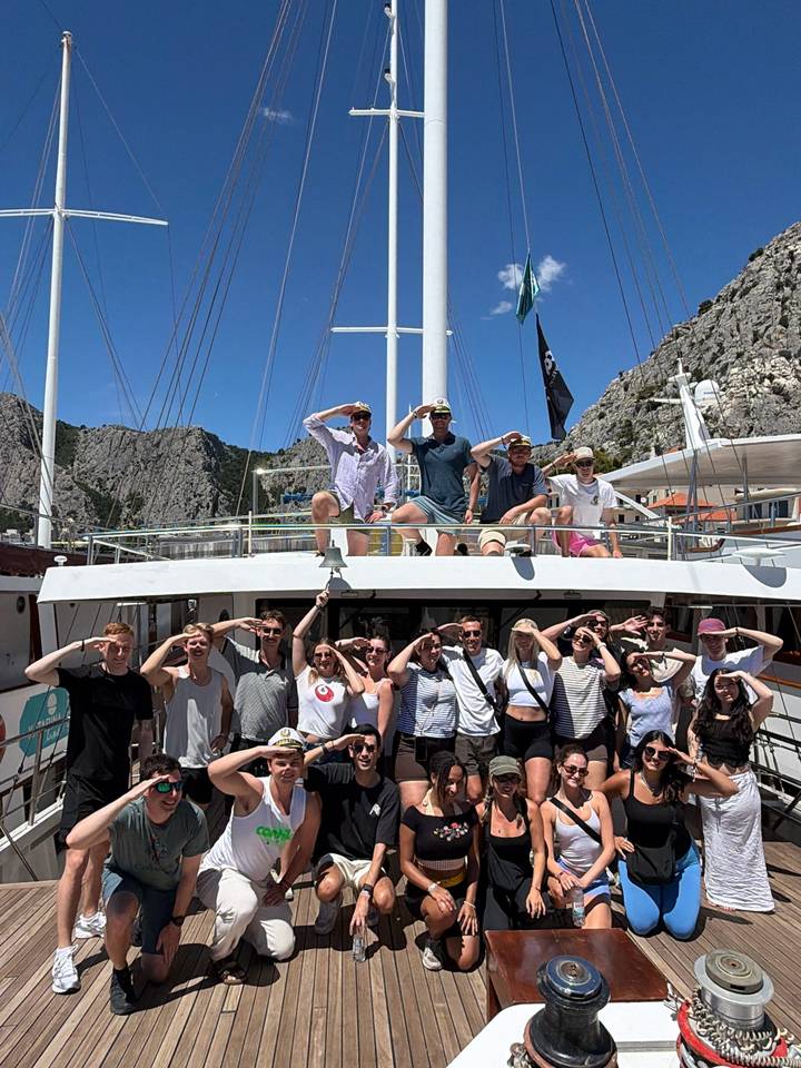 Cheerful group of young travelers saluting on the deck of a small cruise boat