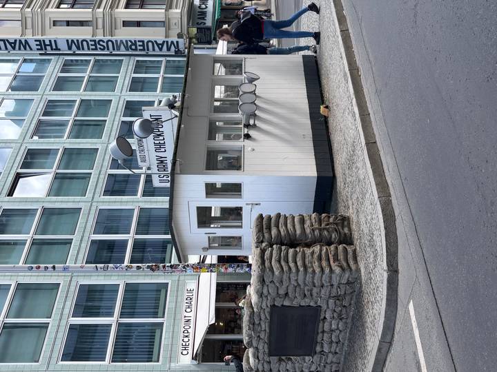 Historic Checkpoint Charlie guardhouse with sandbags and sign on a Berlin street corner.