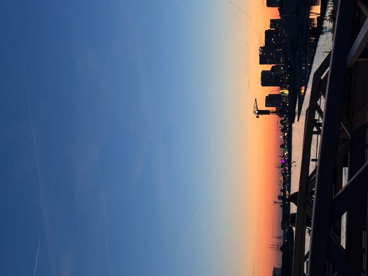 Warm sunset over a canal with modern buildings, a crane and distant lights along Amsterdam’s waterfront.