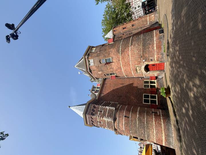 Tall red-brick medieval gatehouse with conical towers and a bright red door against a clear sky.