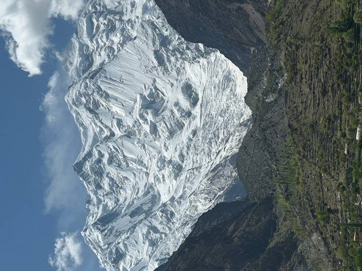 Dramatic, glacier-covered mountain wall towering over a green valley under clear blue sky.