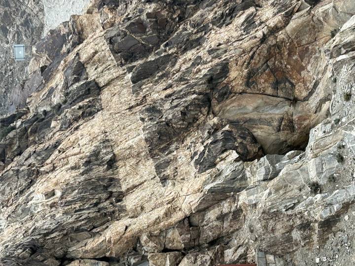 Close-up of rugged rock face with varied colours and a small cave-like opening.