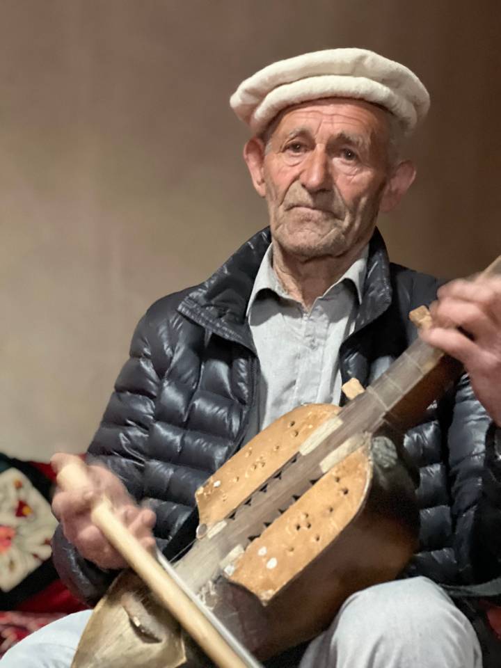Older man playing a traditional string instrument indoors, image slightly out of focus.