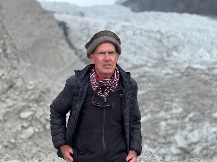 Portrait of traveller in warm clothing with a glacier and rocky landscape behind.