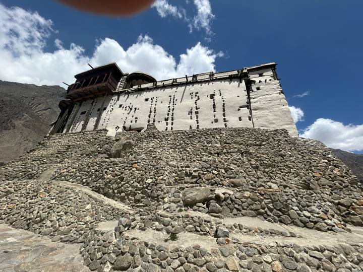 Stone ramparts leading up to the white-walled Baltit Fort against a blue sky.