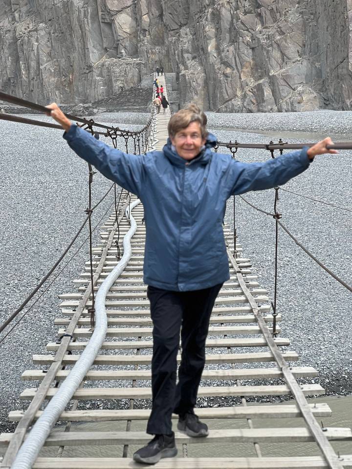 Motion-blurred traveller spreading arms while crossing a narrow suspension bridge.