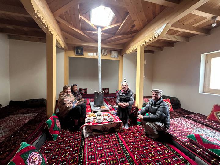 Group enjoys tea and snacks while seated on colourful carpets inside a traditional home.