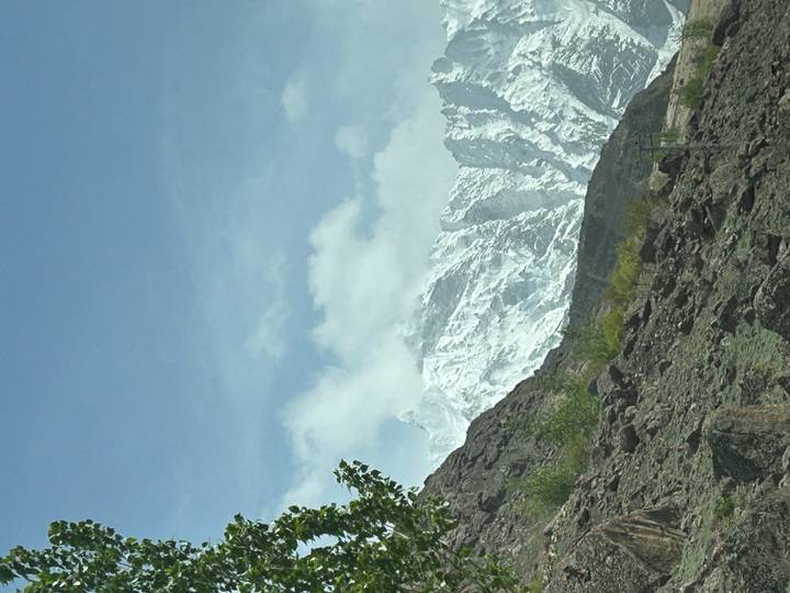 Snow-dusted mountain ridge emerging behind rocky slopes under a pale sky.