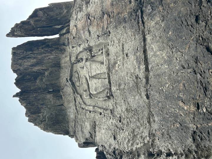 Ancient Buddha figure carved into a tall, dark rock cliff.