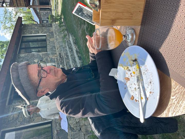 Traveller wearing a traditional cap sits outdoors at a table after a meal, holding a tablet.