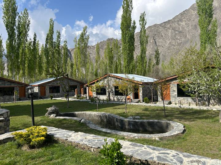 Stone cottages and manicured lawns with a small pond set against tall poplar trees and mountains.